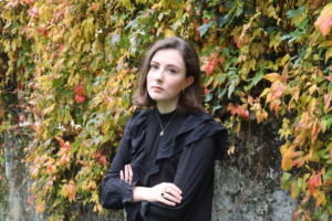 Eilish Mulholland headshot - Eilish standing cross-armed against an ivy covered wall