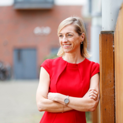 Photo of Breda wearing a red dress standing with her arms crossed smiling 