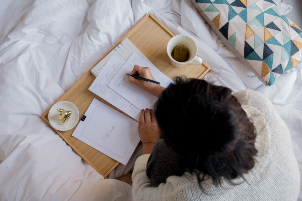 Woman with brown hair sitting with a tray in bed writing on paper