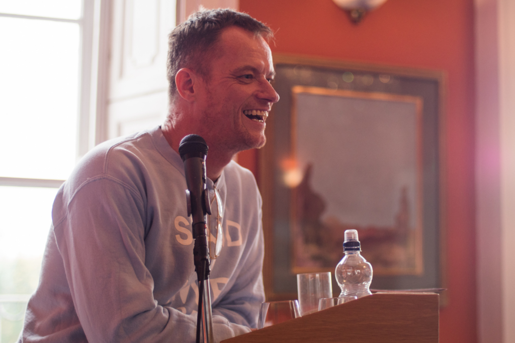 Image of man standing on a podium smiling with a microphone 