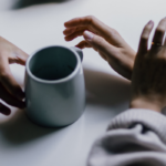photo of hands and a cup of coffee across a table