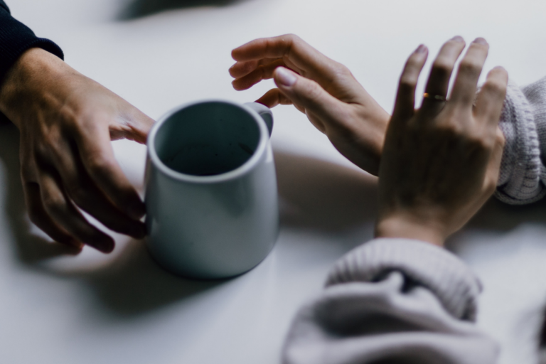 photo of hands and a cup of coffee across a table