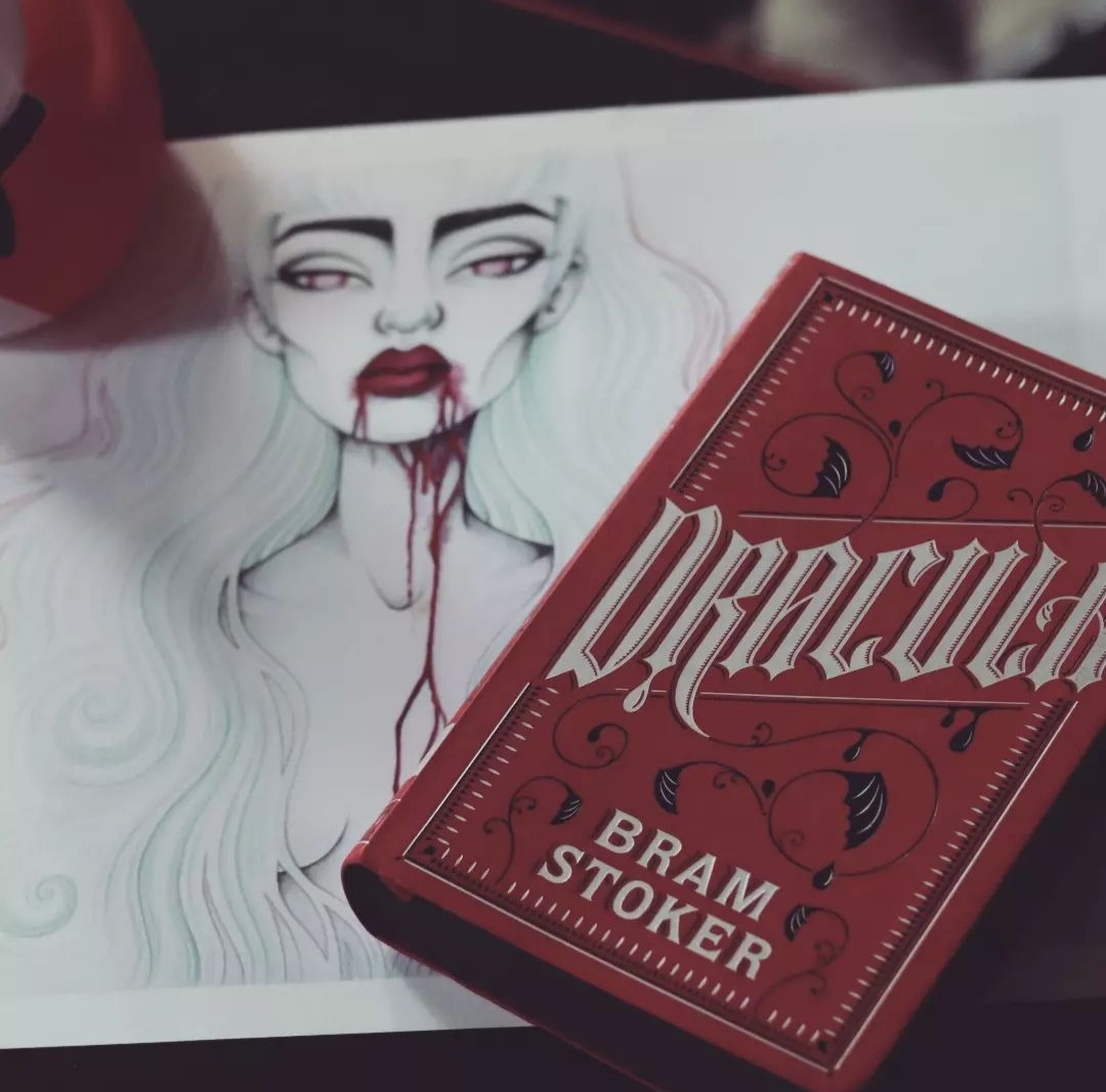 Foreground: Hardback copy of Dracula by Bram Stoker   Background: illustration of a female figure dripping with red blood dripping from her mouth